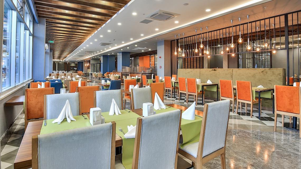 Innenansicht des Restaurants im Saturn Palace Resort mit farbenfrohen Stühlen und Tischen.