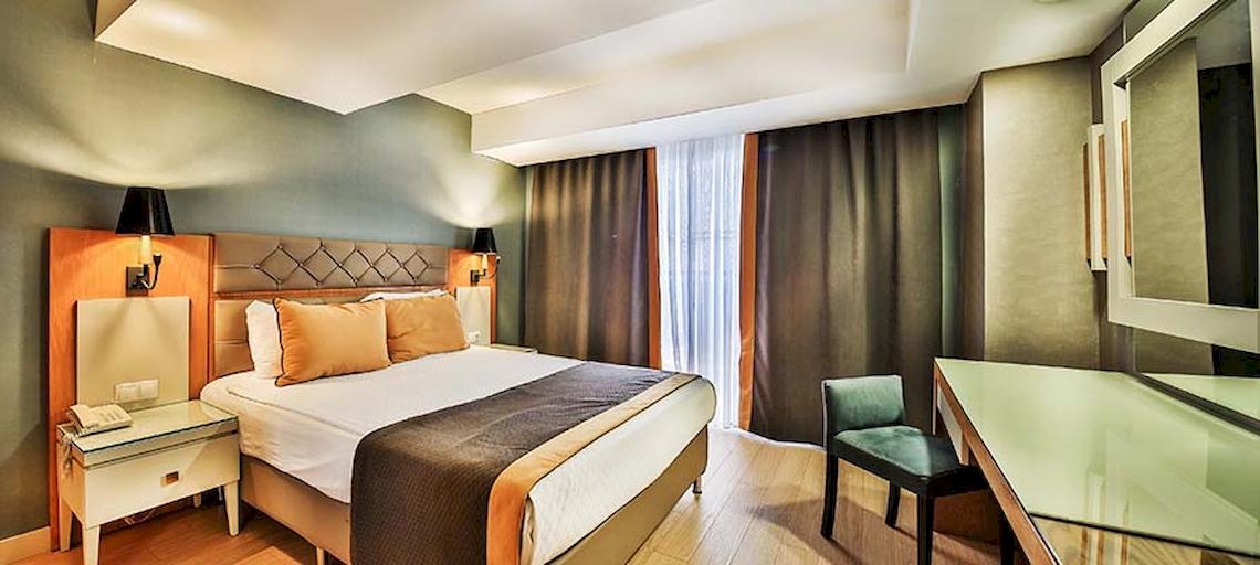 Ein modernes Hotelzimmer im Saturn Palace Resort mit einem großen Bett, Nachttischen, einem Schreibtisch und einem Stuhl.