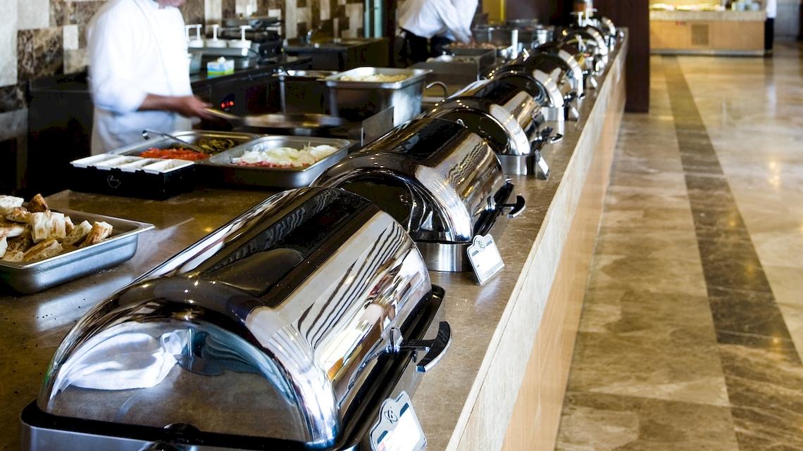 Buffet-Tisch im Saturn Palace Resort mit verschiedenen Speisen und Kellnern im Hintergrund.