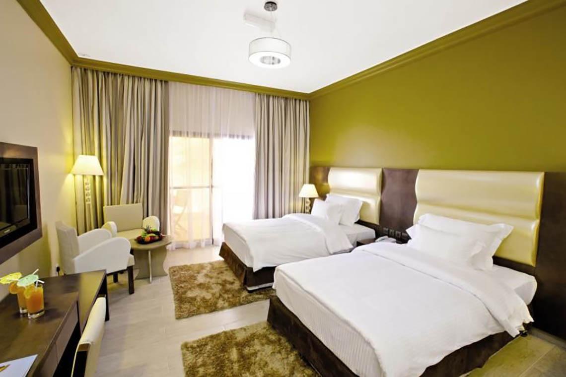 Doppelzimmer im BM Beach Hotel mit zwei Betten, grünen Wänden und weißem Bettzeug.