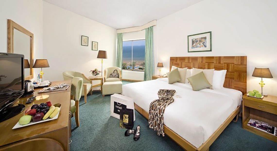 Innenansicht eines Zimmers im BM Beach Hotel mit Bett, Schreibtisch, Fernseher und Fenster mit Meerblick.
