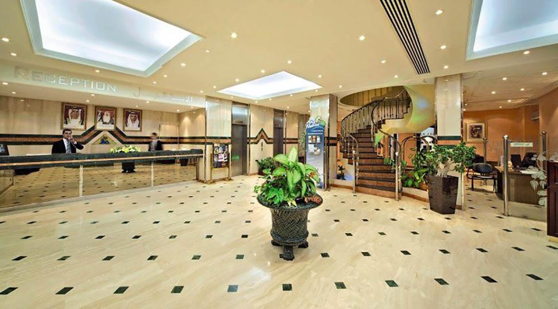 Empfangshalle des BM Beach Hotels mit Marmorboden, Pflanzen und Rezeption im Hintergrund.