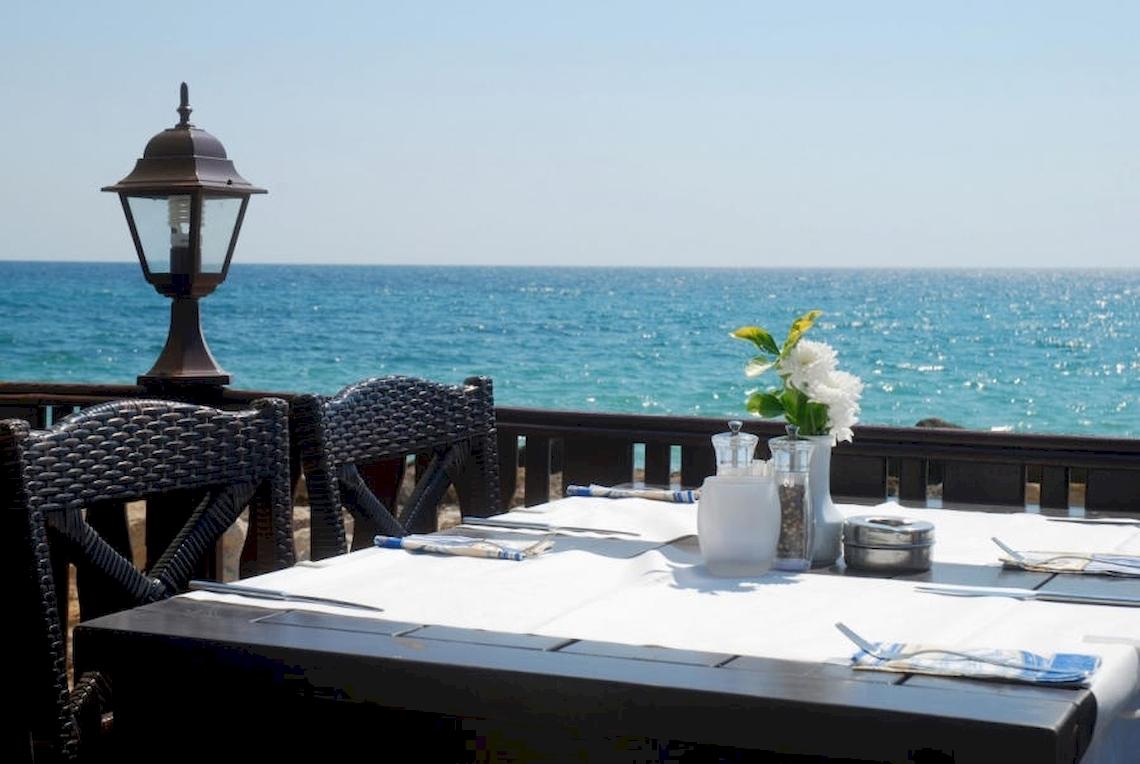 Tisch mit Meerblick im Riviera Beach Hotel, gedeckt mit Tischdecke, Besteck und Blumen.