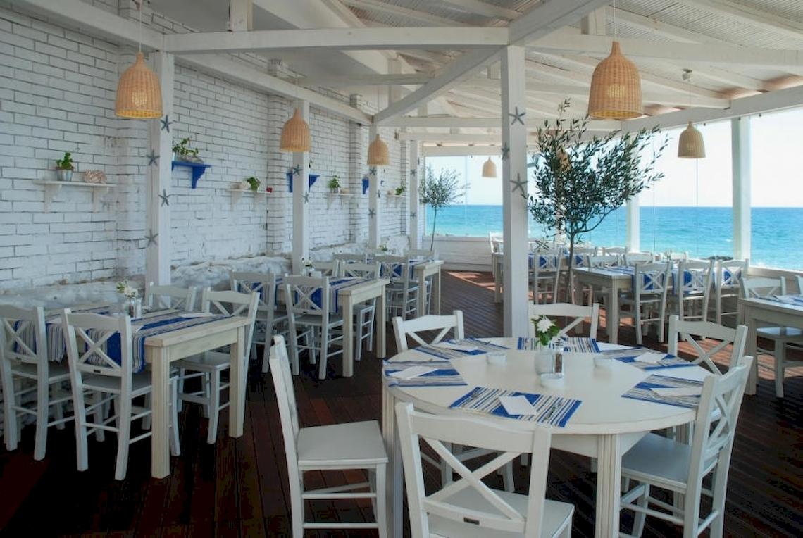 Hotel Terrasse mit Blick auf das Meer und weißen Tischen und Stühlen.