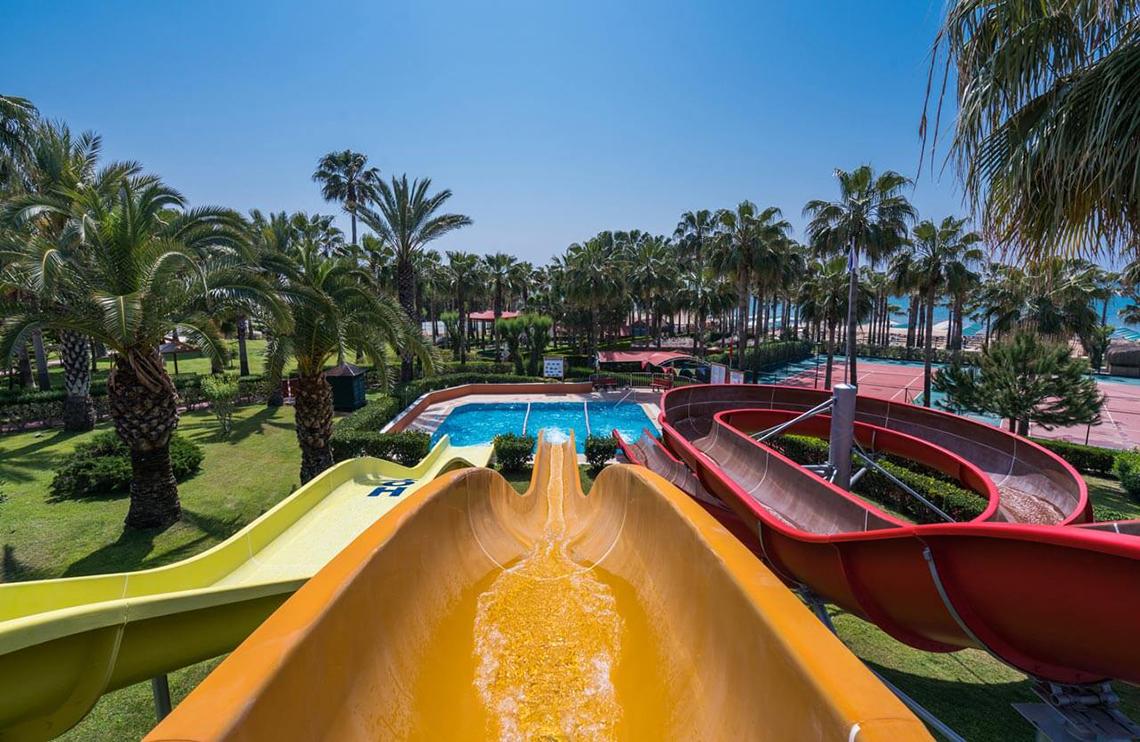 Wasserrutschen im Freien im Miramare Queen Hotel, umgeben von Palmen und einem Pool.
