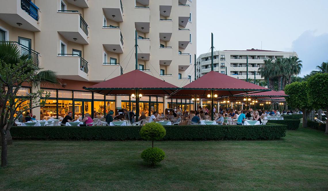 Miramare Queen Hotel Außenterrasse mit Gästen und roten Sonnenschirmen.