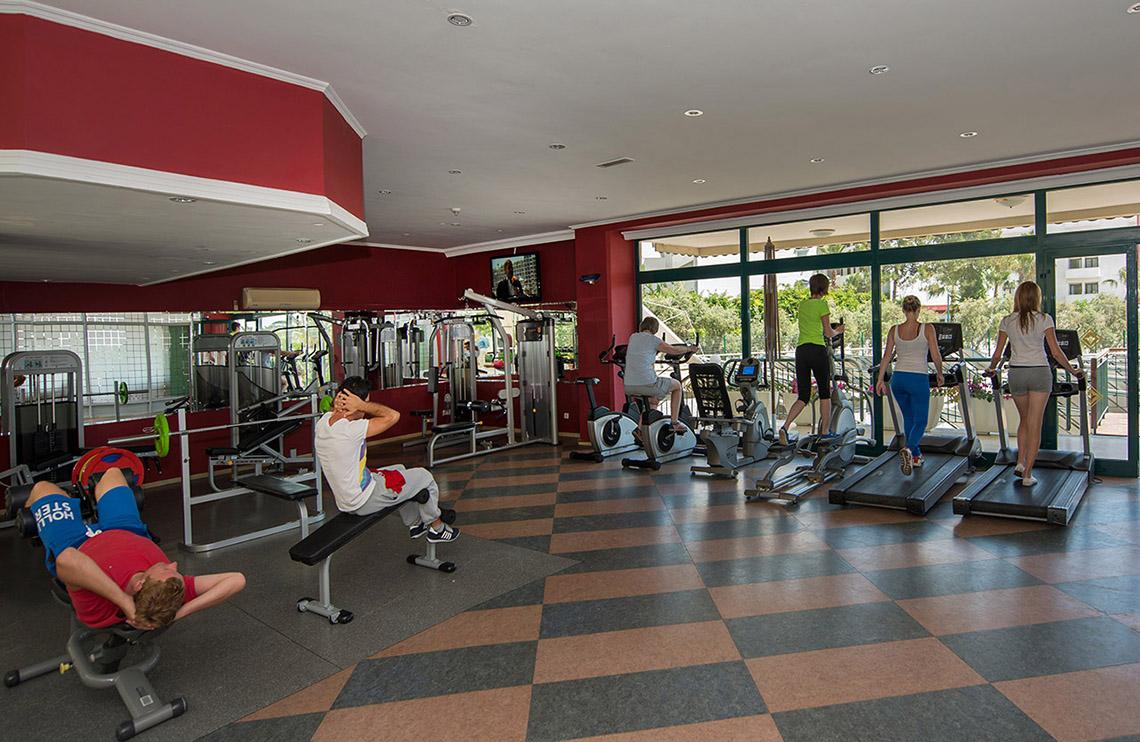 Fitnessstudio im Miramare Queen Hotel mit verschiedenen Trainingsgeräten und Personen, die trainieren.