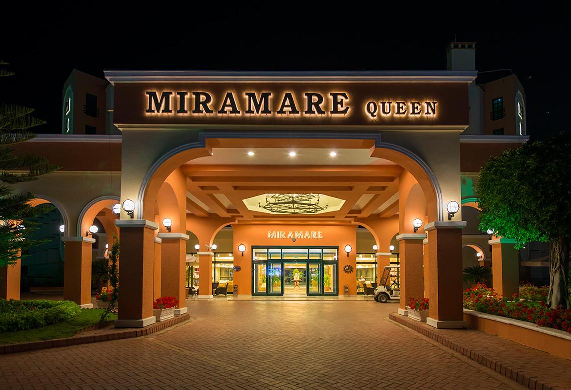 Foto des Miramare Queen Hotels, das bei Nacht beleuchtet ist, mit illuminierten Säulen und eingelassenen Laternen.