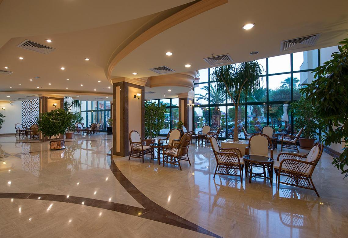 Lobby des Miramare Queen Hotels mit Möbeln, Pflanzen und großen Fenstern.