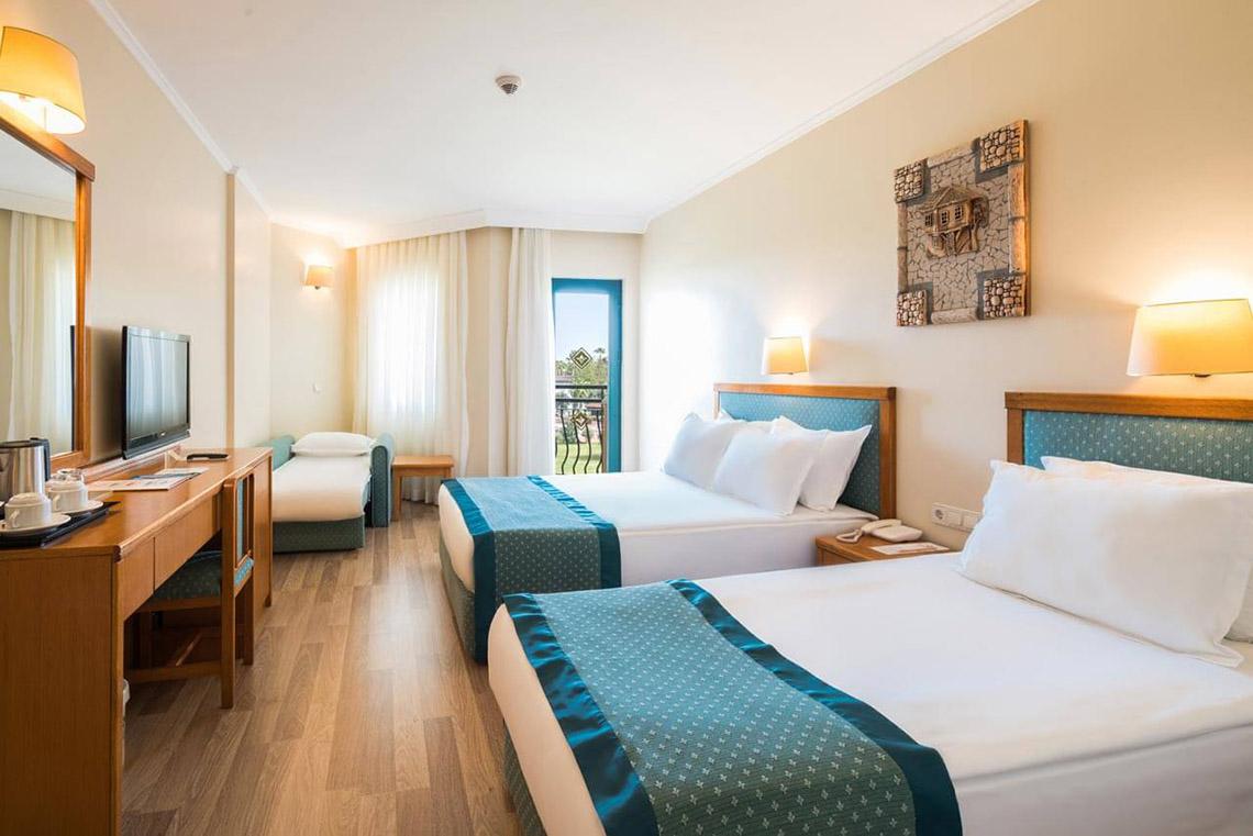 Zwei Doppelbetten in einem geräumigen Hotelzimmer des Miramare Queen, mit einem Schreibtisch und Fernseher.