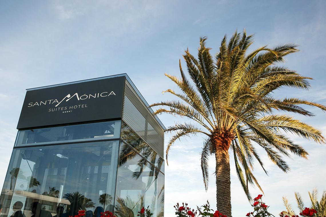 Eingangsbereich des Santa Monica Suites Hotels mit Glasfassade und Palme im Vordergrund.