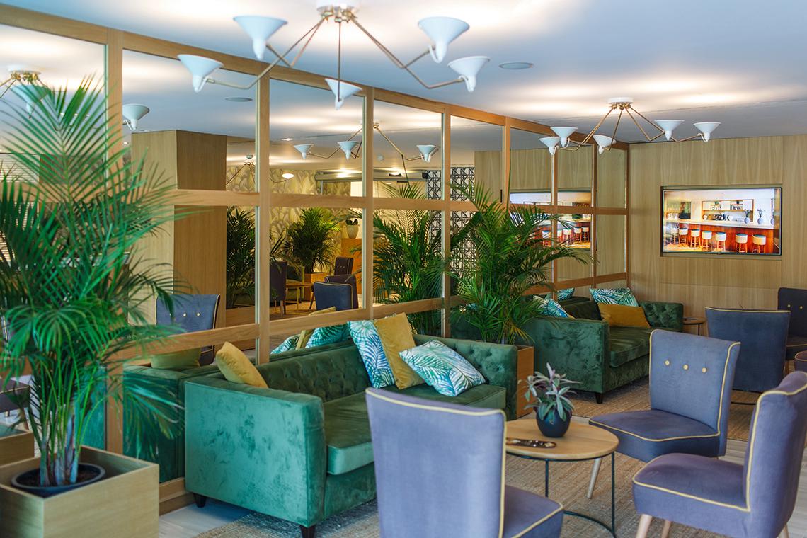 Lobby-Lounge im Santa Monica Suites mit grünen Sofas, Pflanzen und spiegelnden Wänden.