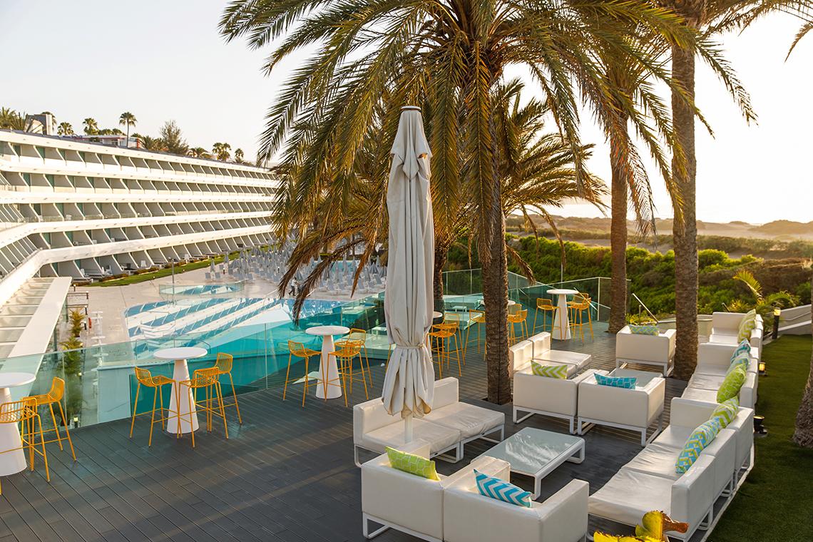 Pool-Terrasse des Santa Monica Suites Hotels mit weißen Möbeln und gelben Stühlen.