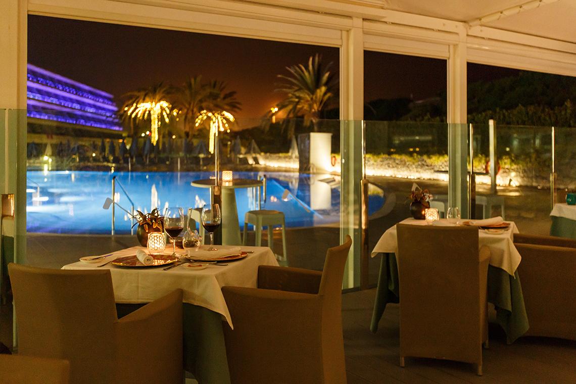 Ein abendlicher Blick auf das Hotelrestaurant von Santa Monica Suites mit Tischen und Stühlen, die den Pool überblicken.