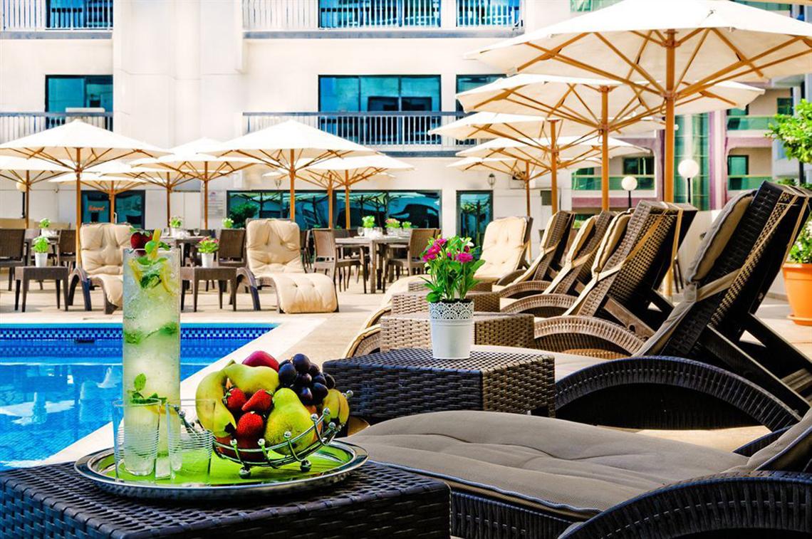 Außenbereich des Golden Sands Hotel Apartments mit Swimmingpool, Sonnenliegen und Schirmen.