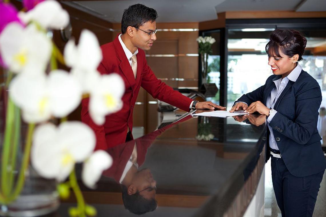Rezeptionist hilft Gast im Golden Sands Hotel Apartments beim Ausfüllen von Unterlagen
