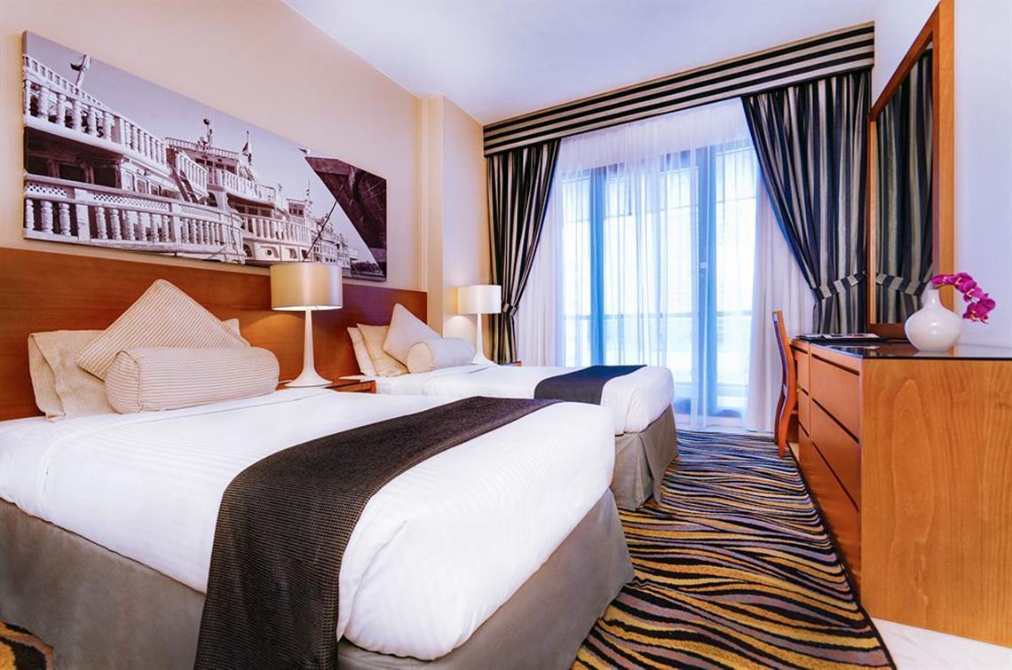 Doppelzimmer im Golden Sands Hotel Apartments mit zwei Betten, Lampen und Panoramafenstern.