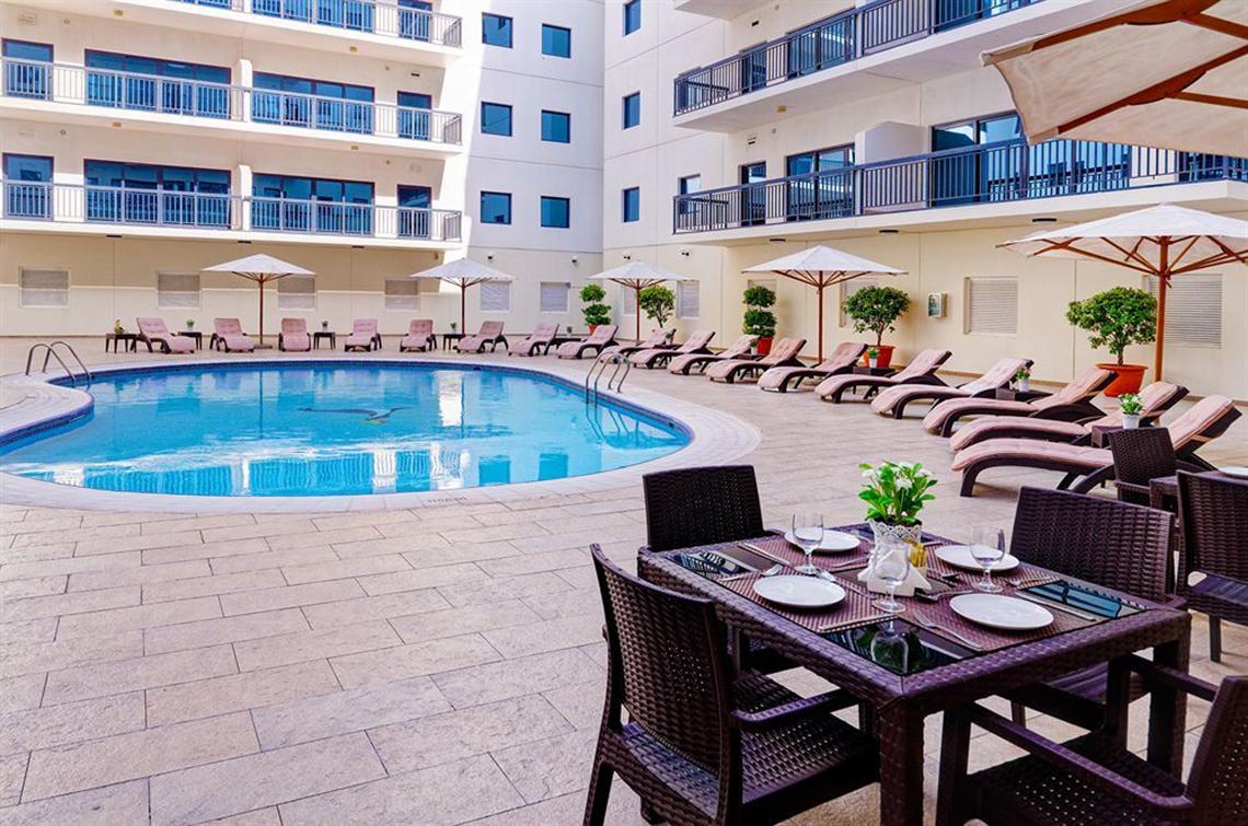 Poolbereich im Golden Sands Hotel Apartments mit Sonnenliegen und Esstisch