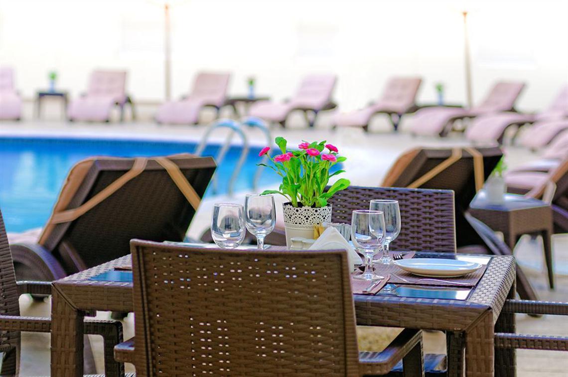 Gartentisch mit Blumen und Strandliegen am Pool des Golden Sands Hotel Apartments