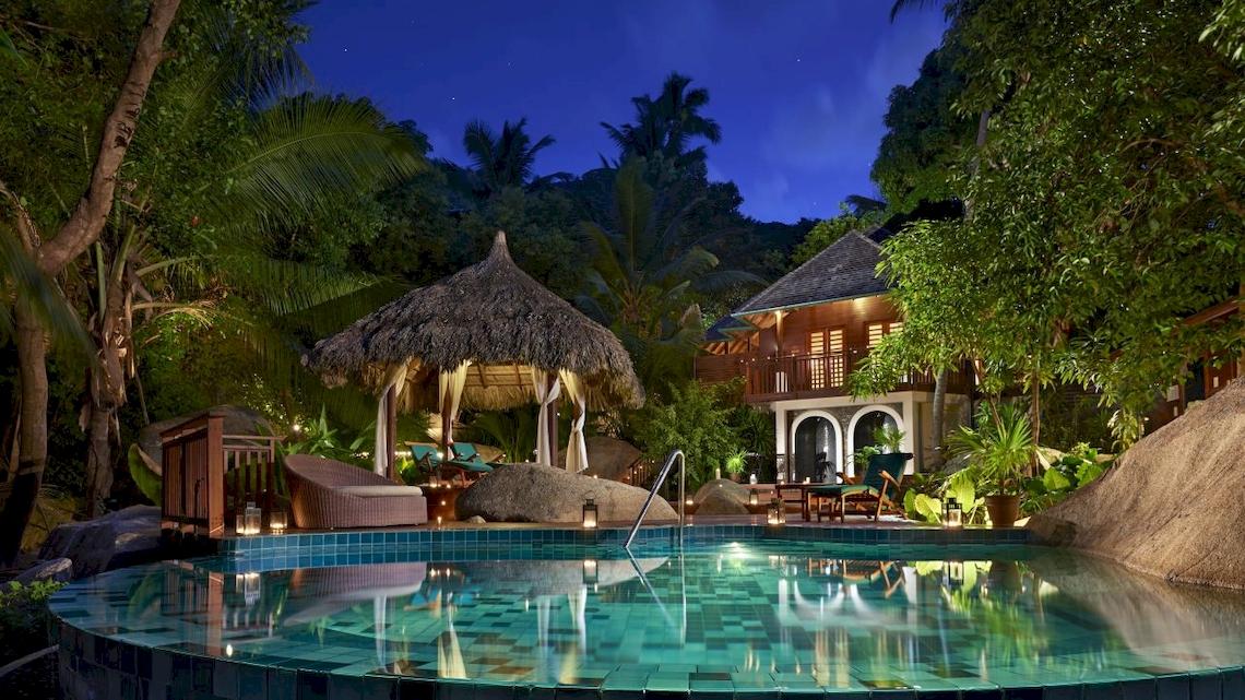 Nachtansicht des Hilton Seychelles Labriz Resorts und Spa mit einem Pool, einem Pavillon und einem Gebäude, umgeben von Bäumen und Pflanzen.