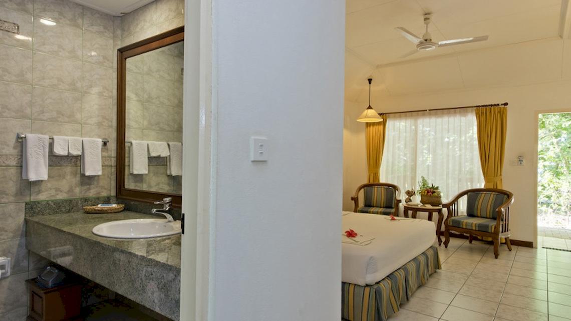 Ein Badezimmer im Royal Island Resort & Spa mit einem Waschbecken, Spiegel, Handtüchern, einem Bett, Stühlen und einer Terrasse.