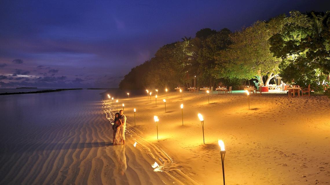 Paar auf einem sandigen Strand des Royal Island Resorts und Spa bei Nacht mit vielen brennenden Fackeln
