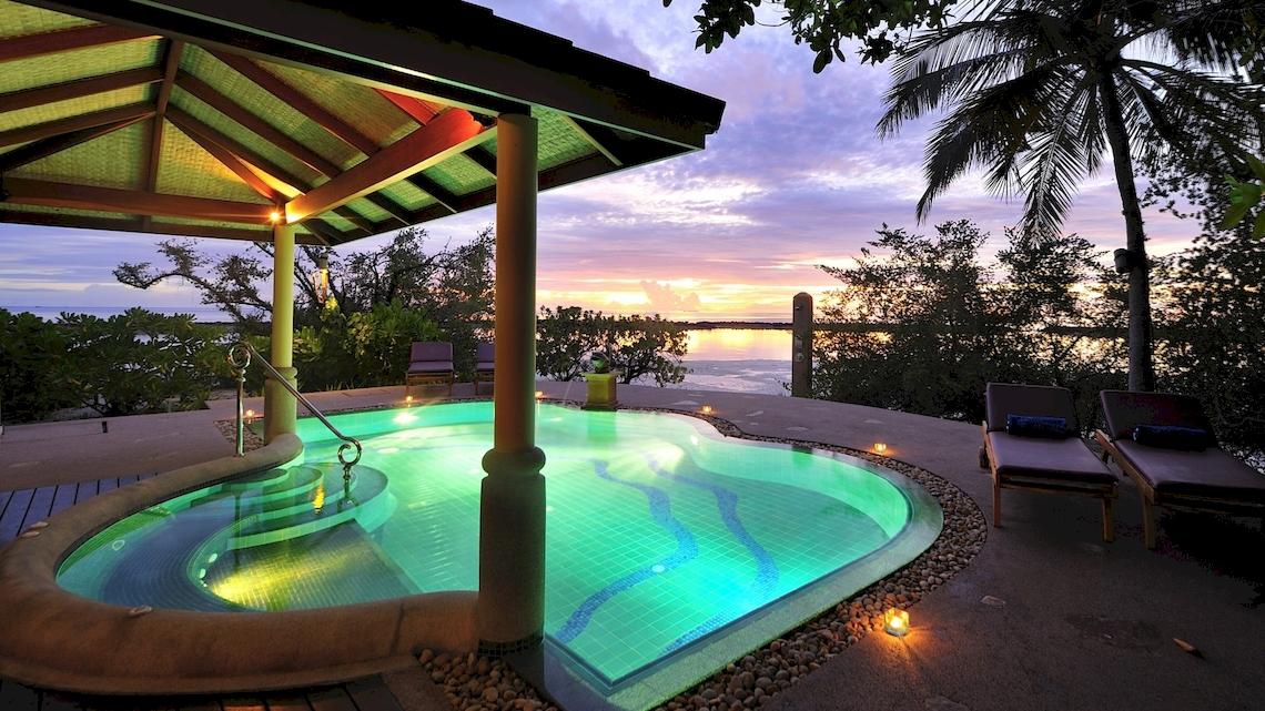 Abendlicher Blick auf den Infinity-Pool des Royal Island Resort & Spa mit beleuchteten Stufen und Lounge-Sesseln.