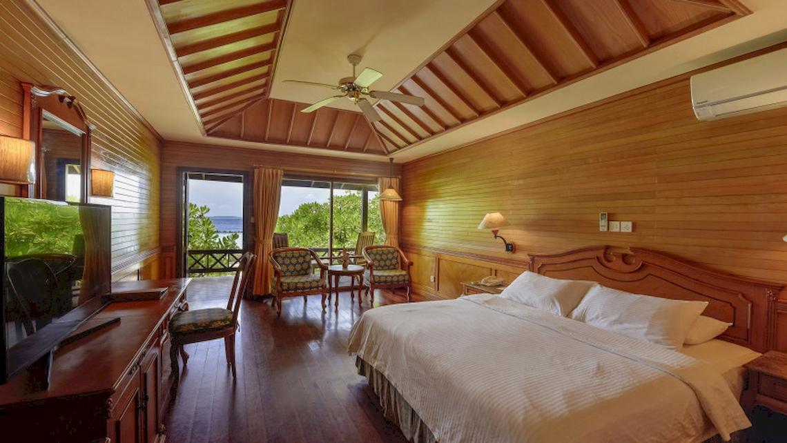 Schlafzimmer im Royal Island Resort & Spa mit Doppelbett, Fernseher, Holzmöbeln und Terrassenzugang.
