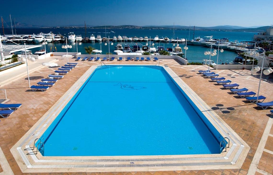Luftaufnahme des Pools im Altin Yunus Hotel & Spa mit vielen Liegestühlen und Booten im Hafen.