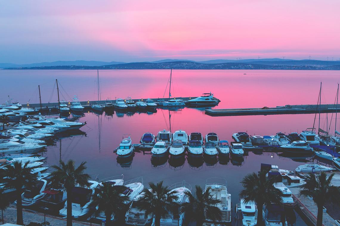 Ein Hafen mit vielen weißen Booten, die bei einem pinkfarbenen Sonnenuntergang verankert sind.