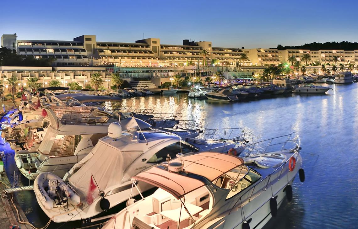 Ein Hotel namens Altin Yunus Hotel & Spa, das viele Boote im Hafen hat, bei Nacht.