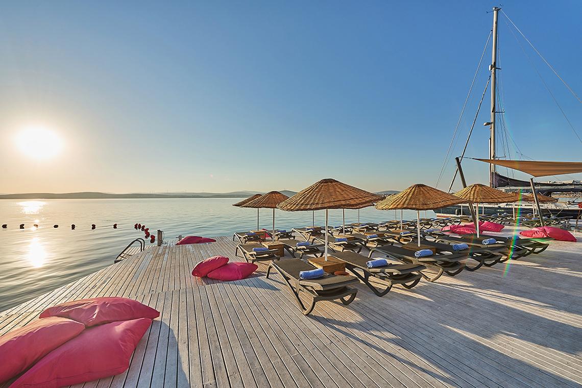 Terrasse des Altin Yunus Hotel & Spa mit Sonnenliegen und Sonnenschirmen am Wasser