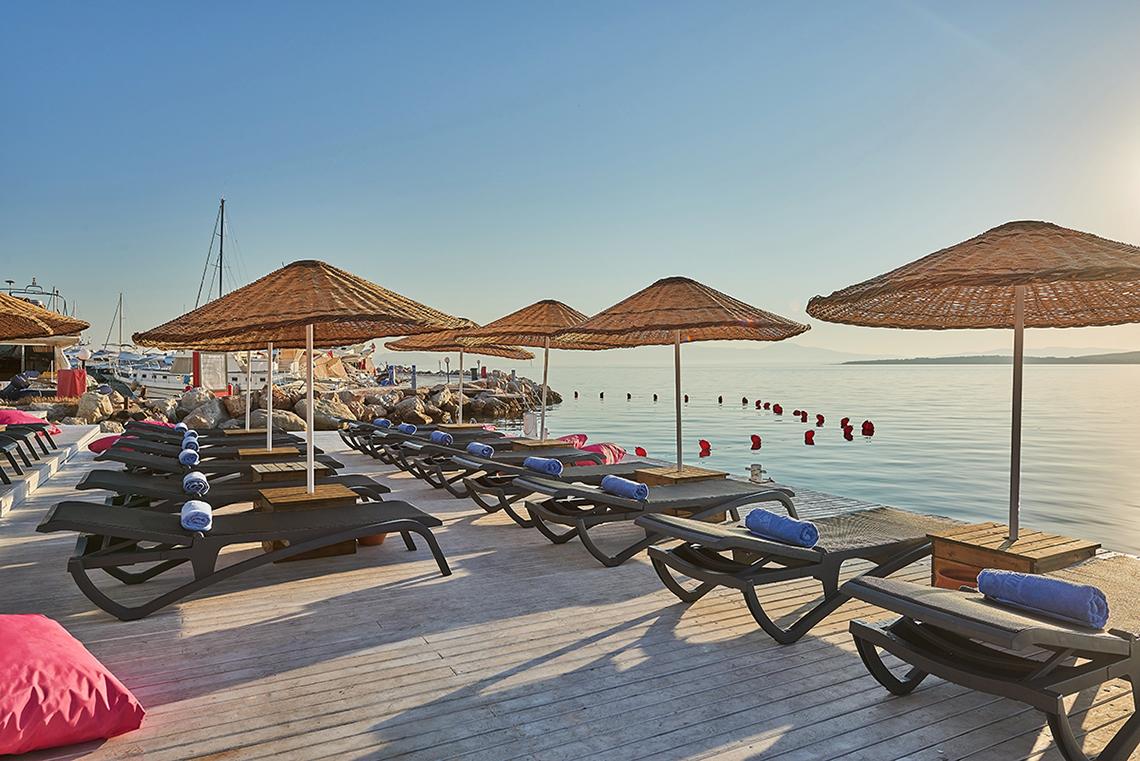 Reihe von Sonnenliegen mit Sonnenschirmen am Strand des Altin Yunus Hotel & Spa.