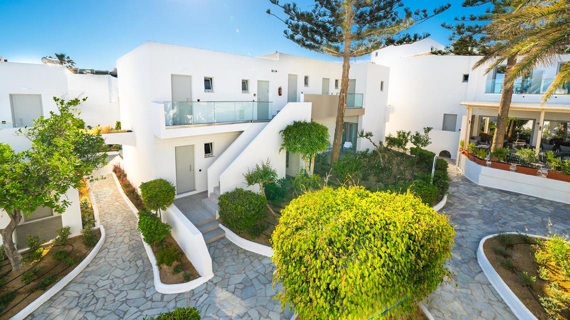 Außenansicht des Adele Beach Hotels mit weißen Gebäuden, Treppen und gepflegten Gärten.
