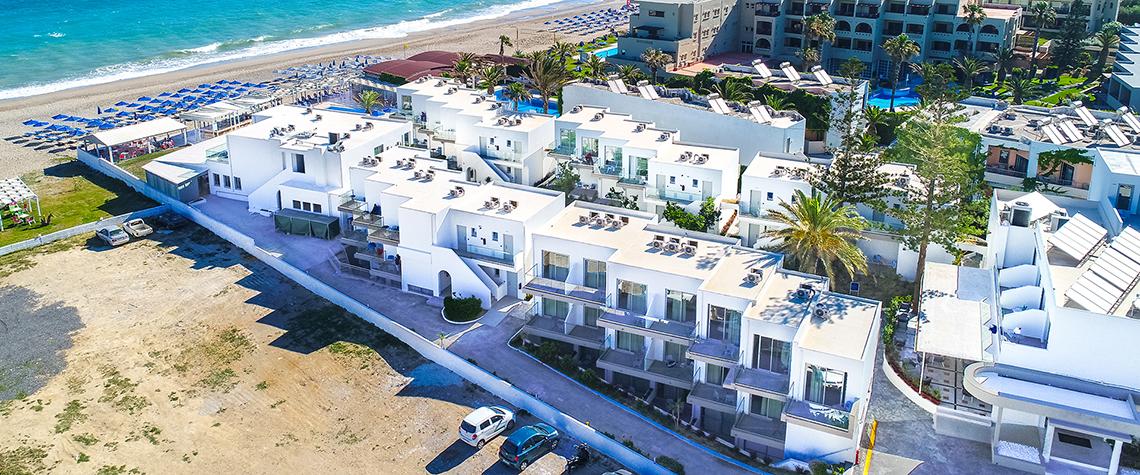 Luftaufnahme des Adele Beach Hotels am Strand mit mehreren Gebäuden und Sonnenliegen.