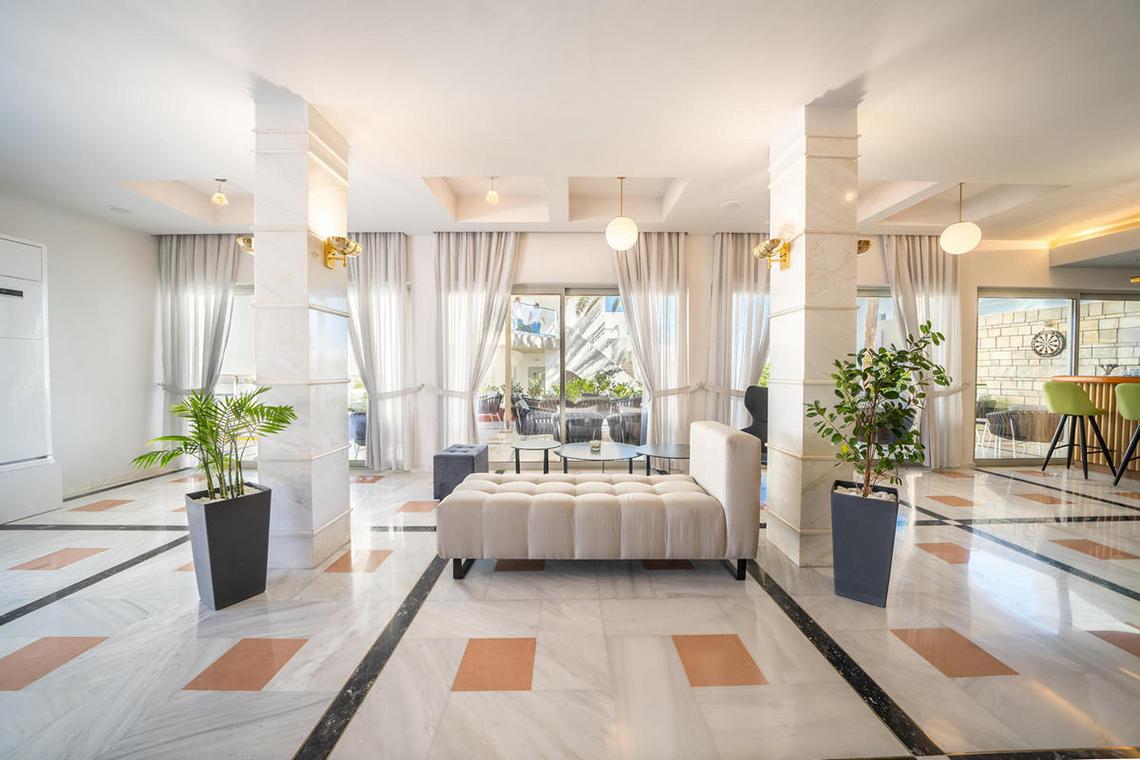 Empfangsbereich des Adele Beach Hotels mit weißem Marmorboden, hohen Säulen und modernen Möbeln.