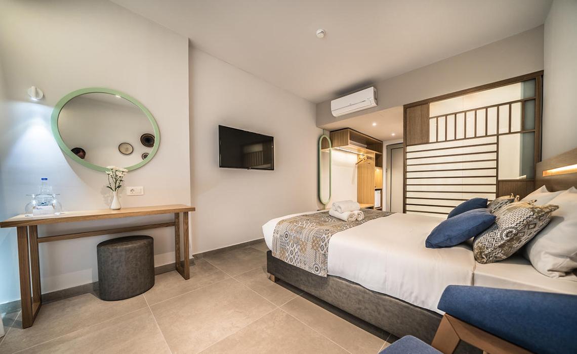 Innenansicht eines Zimmers im Adele Beach Hotel mit Bett, Nachttisch und Spiegel.