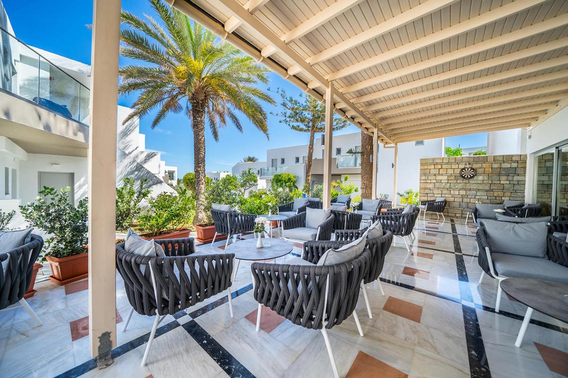 Terrasse des Adele Beach Hotels mit Lounge-Sesseln und Pflanzen, beschattet von einer Pergola.