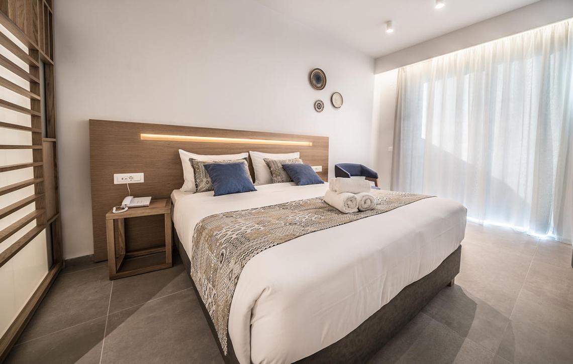 Schlafzimmer im Adele Beach Hotel mit großem Bett, Kissen und Decken, neben einem Nachttisch
