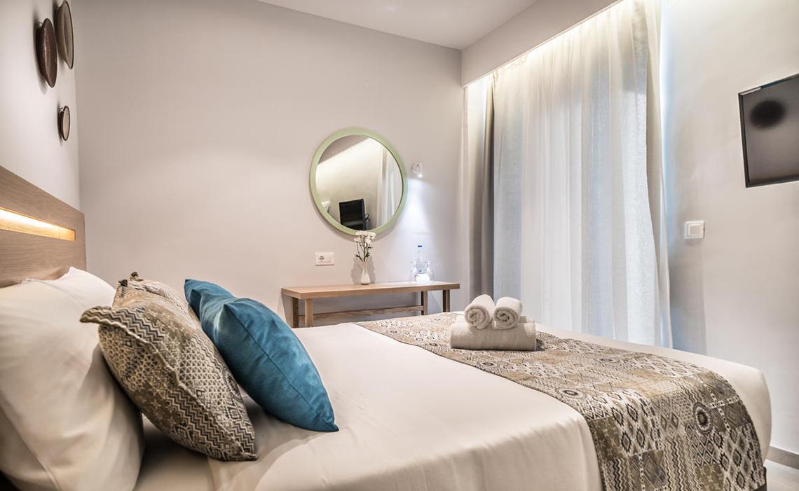 Schlafzimmer im Adele Beach Hotel mit einem Bett, Kissen, Spiegel und Nachttisch.