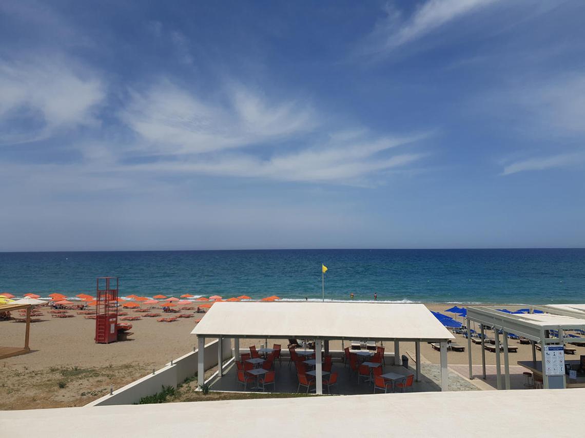 Aussicht vom Adele Beach Hotel auf den Strand mit Sonnenschirmen und Tischen.