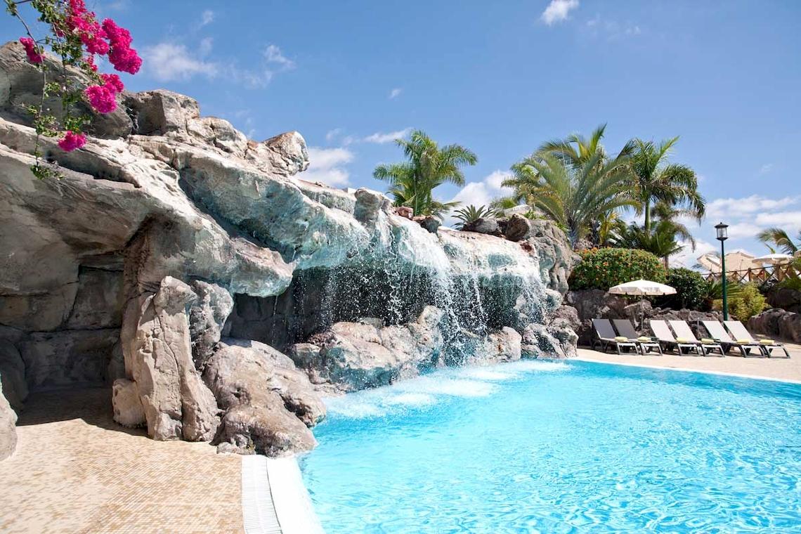 Außenpool mit Wasserfall im Roca Nivaria Gran Hotel mit Liegestühlen und Sonnenschirmen.