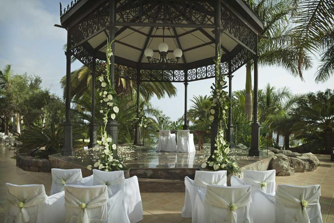 Hochzeitszeremonie im Garten des Roca Nivaria Gran Hotel, umgeben von weißen Stühlen und Blumen.