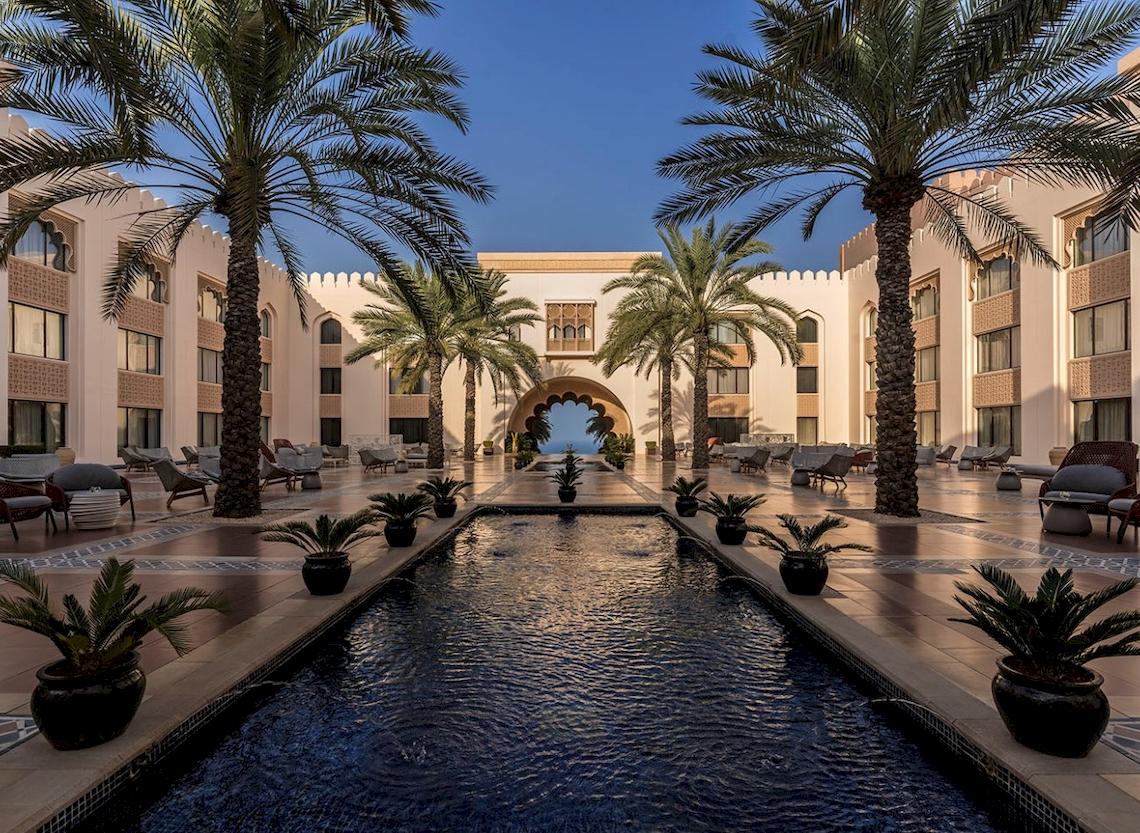 Ein Swimmingpool mit Palmen und Gebäuden im Shangri-La Al Husn Resort & Spa.