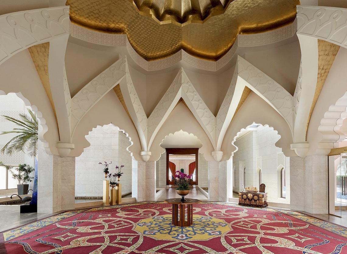 Empfangsbereich des Shangri-La Al Husn Resort & Spa mit rotem Teppich und blumigem Arrangement.