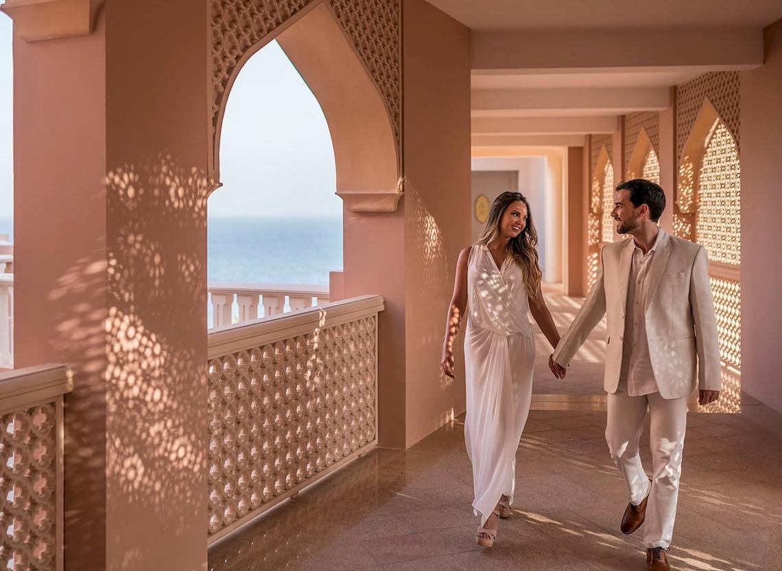 Ein Paar geht auf dem Balkon des Shangri-La Al Husn Resorts & Spa, mit Blick auf das Meer.