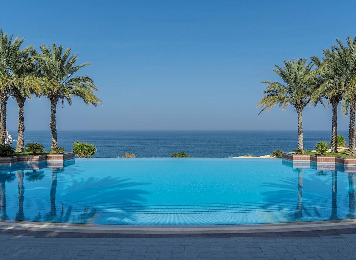 Infinity Pool am Shangri-La Al Husn Resort & Spa mit Blick auf das Meer und Palmen