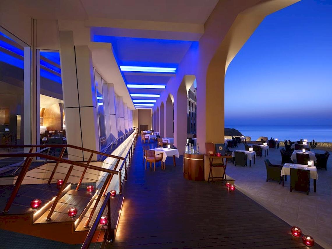 Terrasse des Shangri-La Al Husn Resorts & Spas mit blauen Beleuchtungslichtern, Tischen und Stühlen.