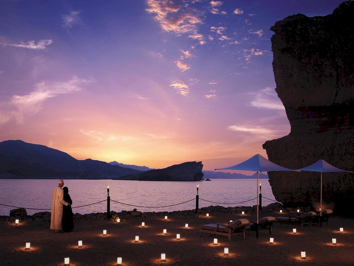 Shangri-La Al Husn Resort & Spa mit romantischem Strand-Setup bei Sonnenuntergang.