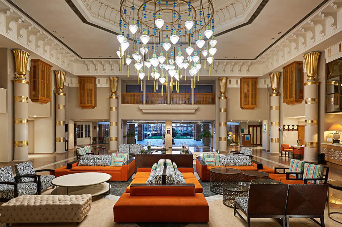Lobby des Continental Hotel Hurghada mit großen Kronleuchter, orangefarbenen Sofas und goldenen Säulen.